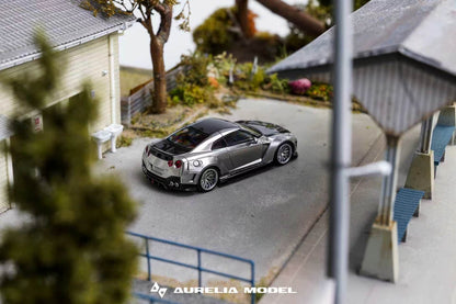 A miniature model of a silver Nissan GT-R R35, manufactured by Aurelia Model, displayed on a detailed miniature street scene with a house, trees, and a station platform.