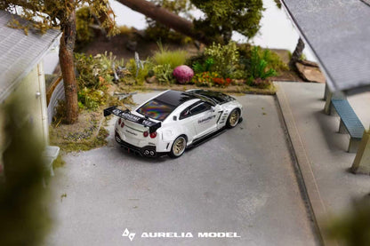 A miniature scale model of a white and black Nissan GT-R Nismo race car, displayed in a detailed diorama setting with a miniature road, trees, and buildings. The brand 'Aurelia Model' is visible as a watermark at the bottom.