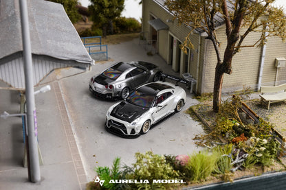 A miniature diorama model of two silver Nissan GT-R cars parked in a driveway next to a house, with a prominent Aurelia Model logo at the bottom.