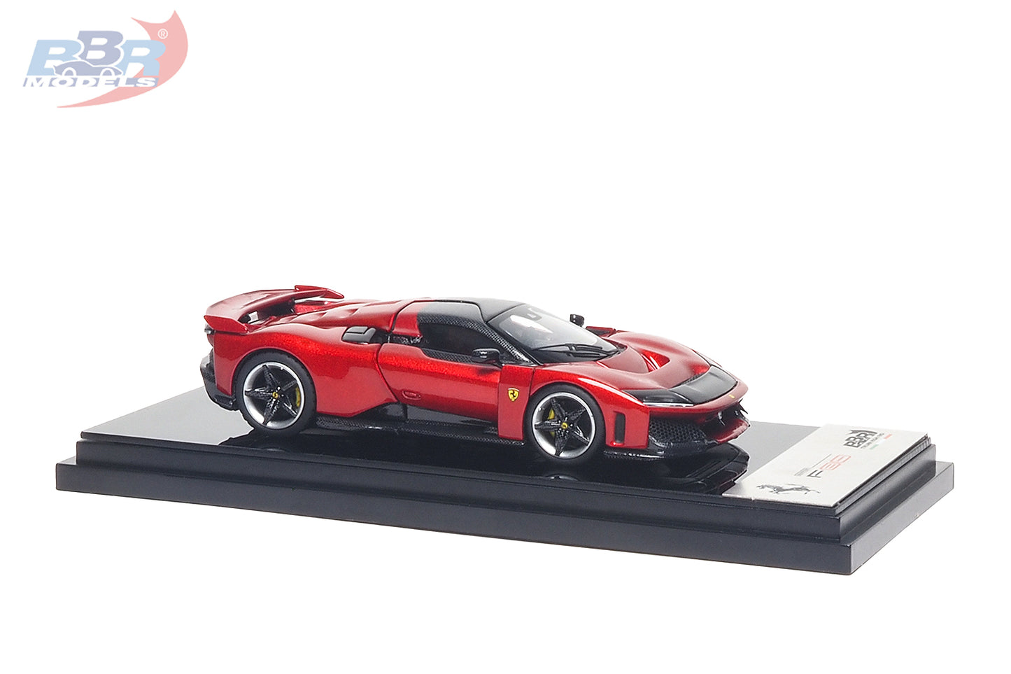 1:64 scale Ferrari F80 diecast model in Rosso Corsa red displayed on a premium black presentation base, shown from the front three-quarter angle. Features carbon fiber accents, sculpted aerodynamic bodywork, realistic alloy wheels with yellow brake calipers, Ferrari shield fender badges, and an aggressive front fascia, making it a premium collectible for Ferrari enthusiasts and diecast model collectors