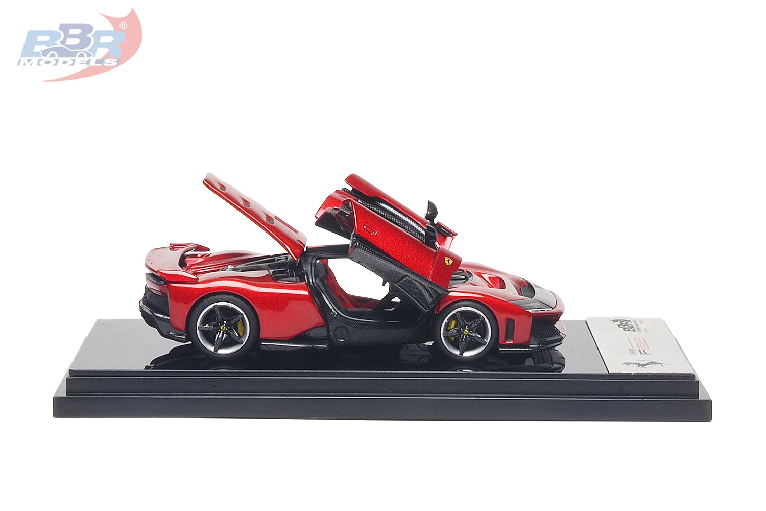 1:64 scale Ferrari F80 diecast model in Rosso Corsa red shown in side profile with the butterfly door and rear engine cover opened, revealing the detailed cockpit and engine bay. Features carbon fiber accents, realistic brake calipers and wheels, aerodynamic styling, and a premium display base, making it a highly detailed collectible for Ferrari enthusiasts and diecast model collectors