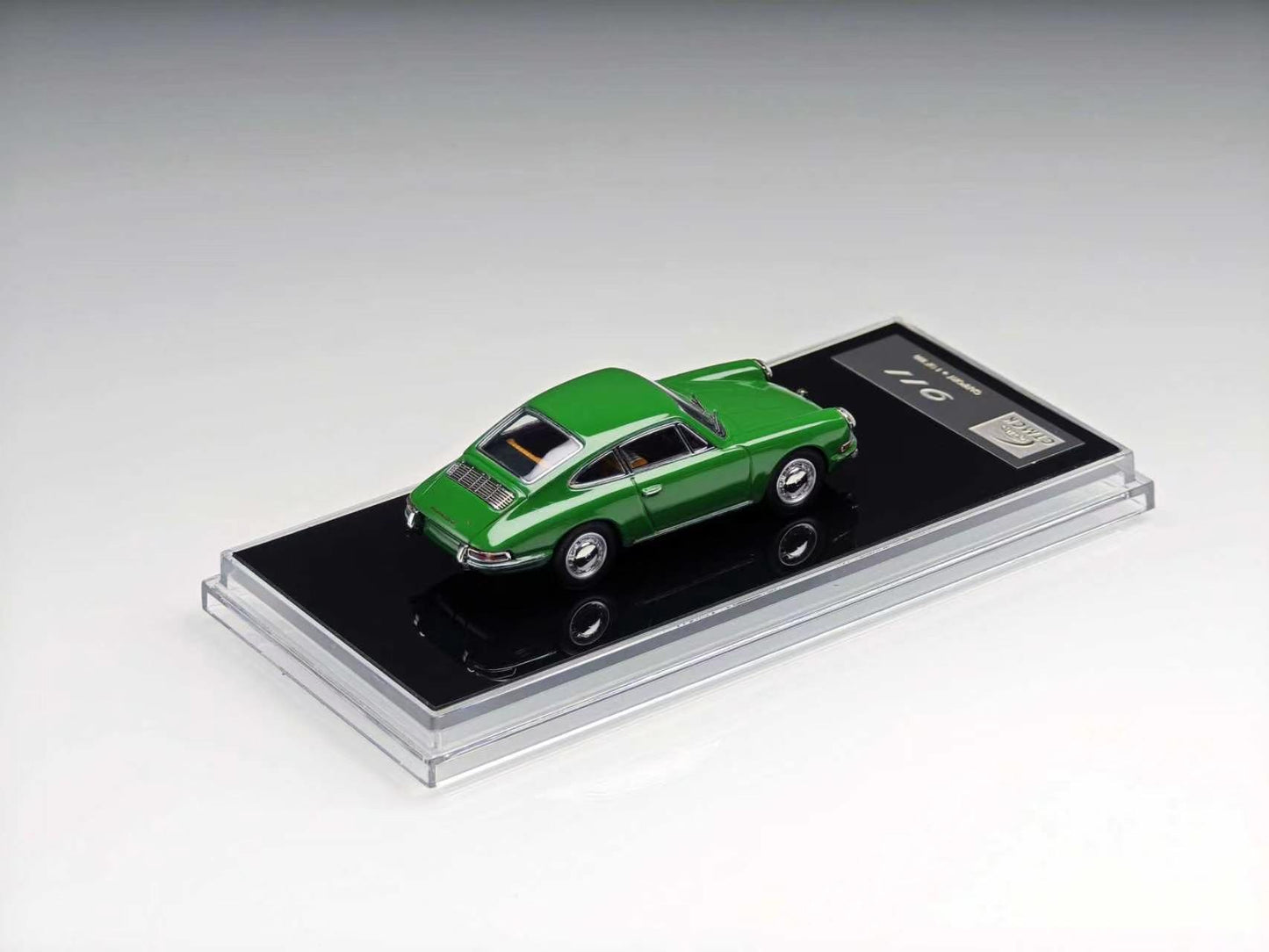 A green vintage sports car model displayed on a black rectangular base inside a clear acrylic case, photographed on a clean light gray studio background.
