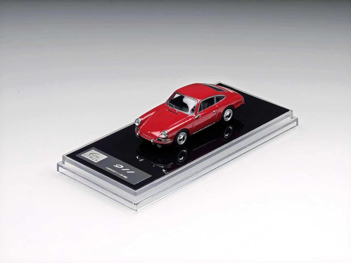 A red miniature model car displayed on a black base inside a clear acrylic case, photographed on a clean light gray studio background.