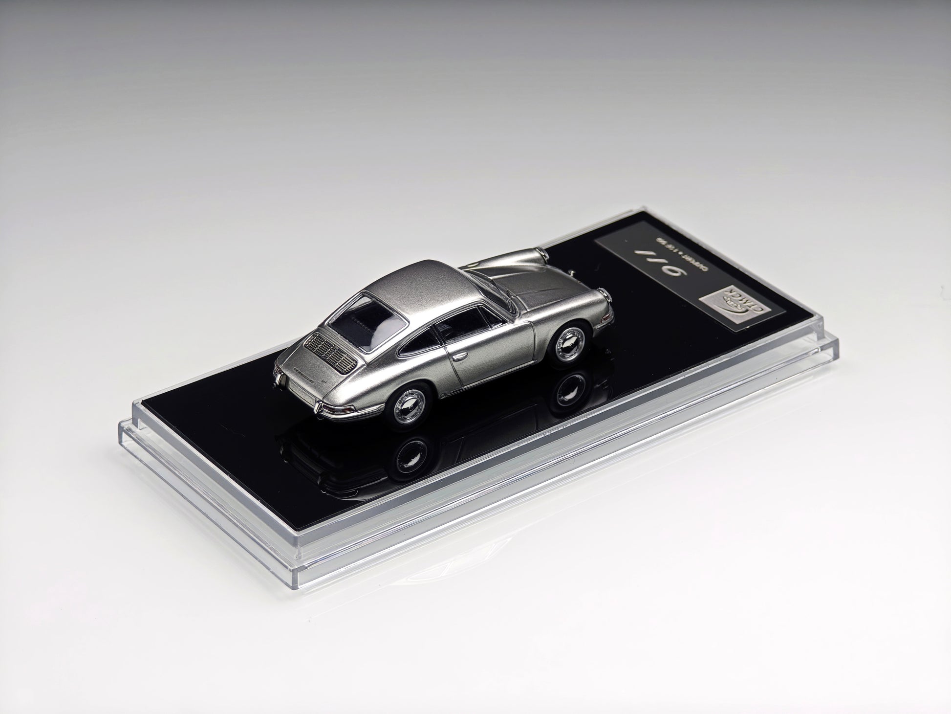 A metallic silver diecast model car displayed on a black base with a clear acrylic cover, photographed on a clean light gray studio background.