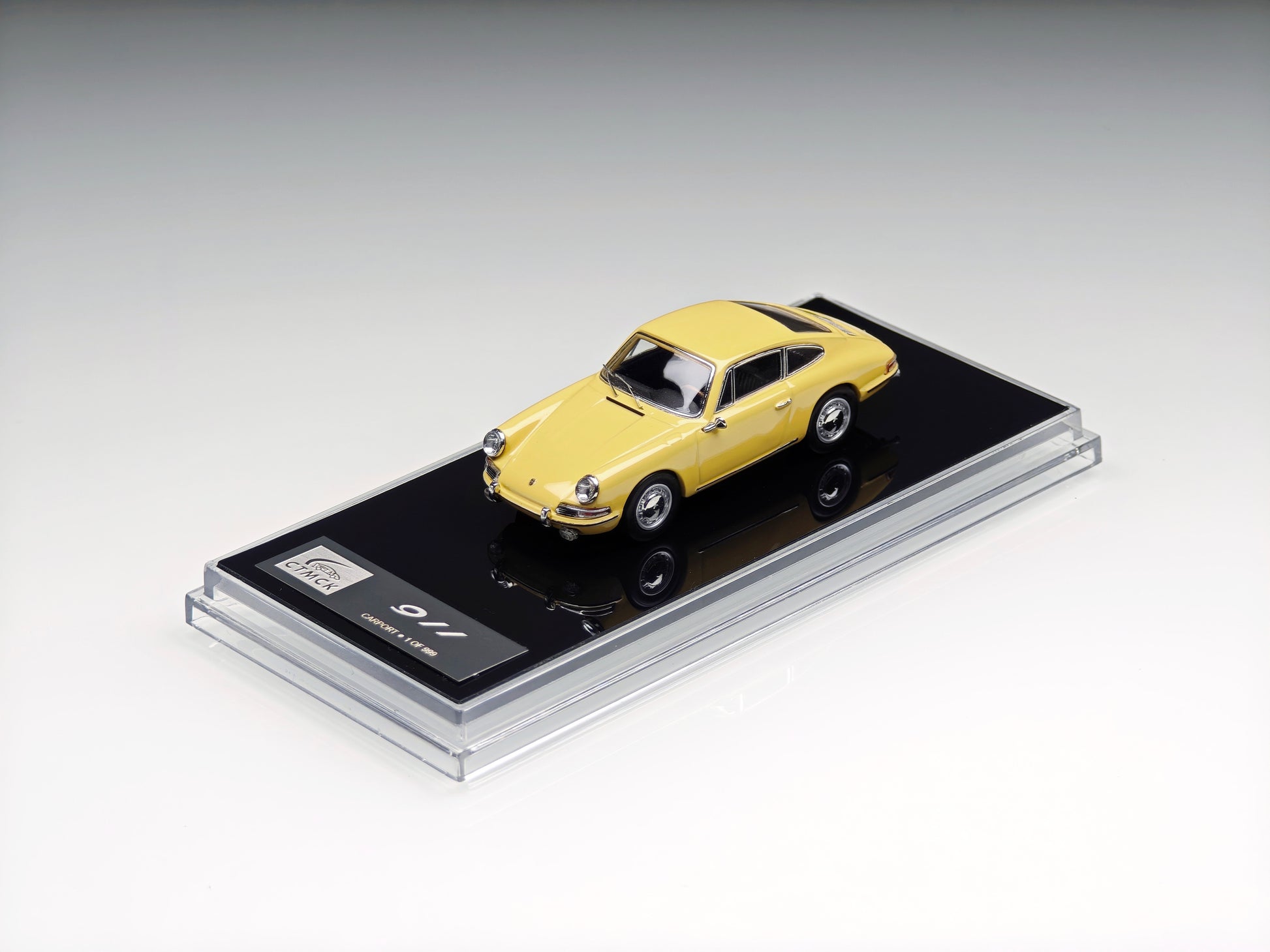 A yellow die-cast model car displayed on a black base inside a clear acrylic case, photographed on a clean light gray studio background.