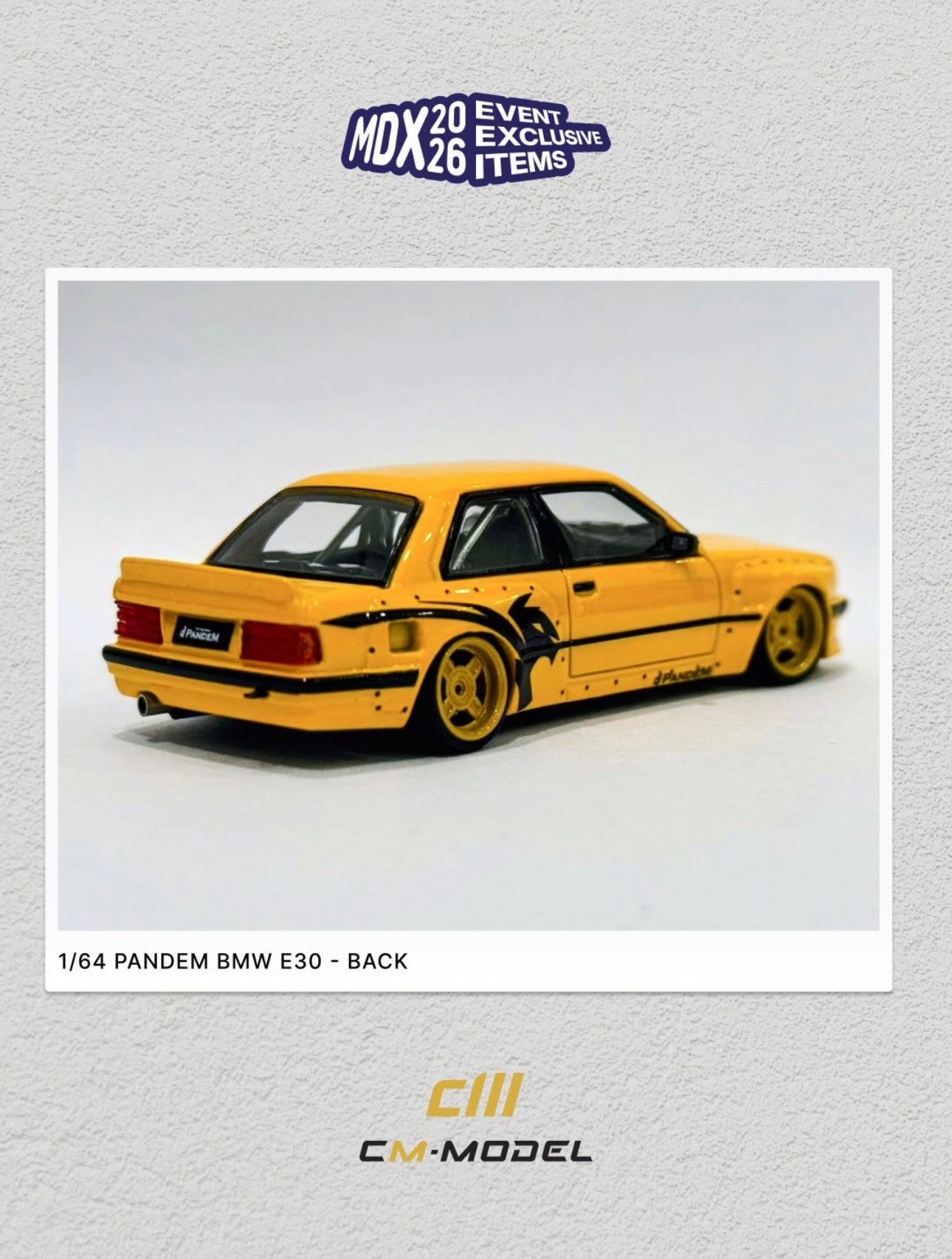 A 1/64 scale model car of a yellow PanDEM BMW E30 from the back, shown inside a white-bordered photo frame on a light gray textured background. The frame includes branding for 'CM-Model' and an 'MDX2026 Event Exclusive Items' badge.