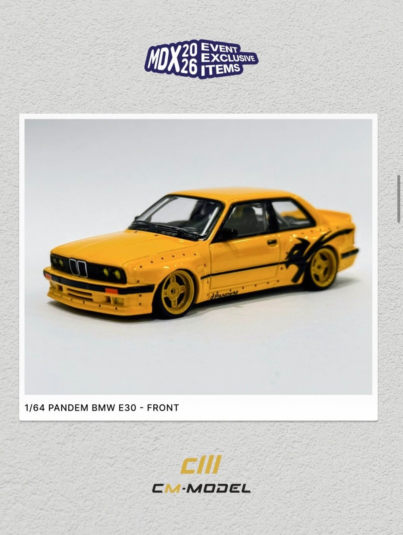 A 1/64 scale model of a yellow and black customized BMW E30, shown from the front. The model is presented on a light gray textured background with promotional text and logos for CM-Model and MDX 2026.