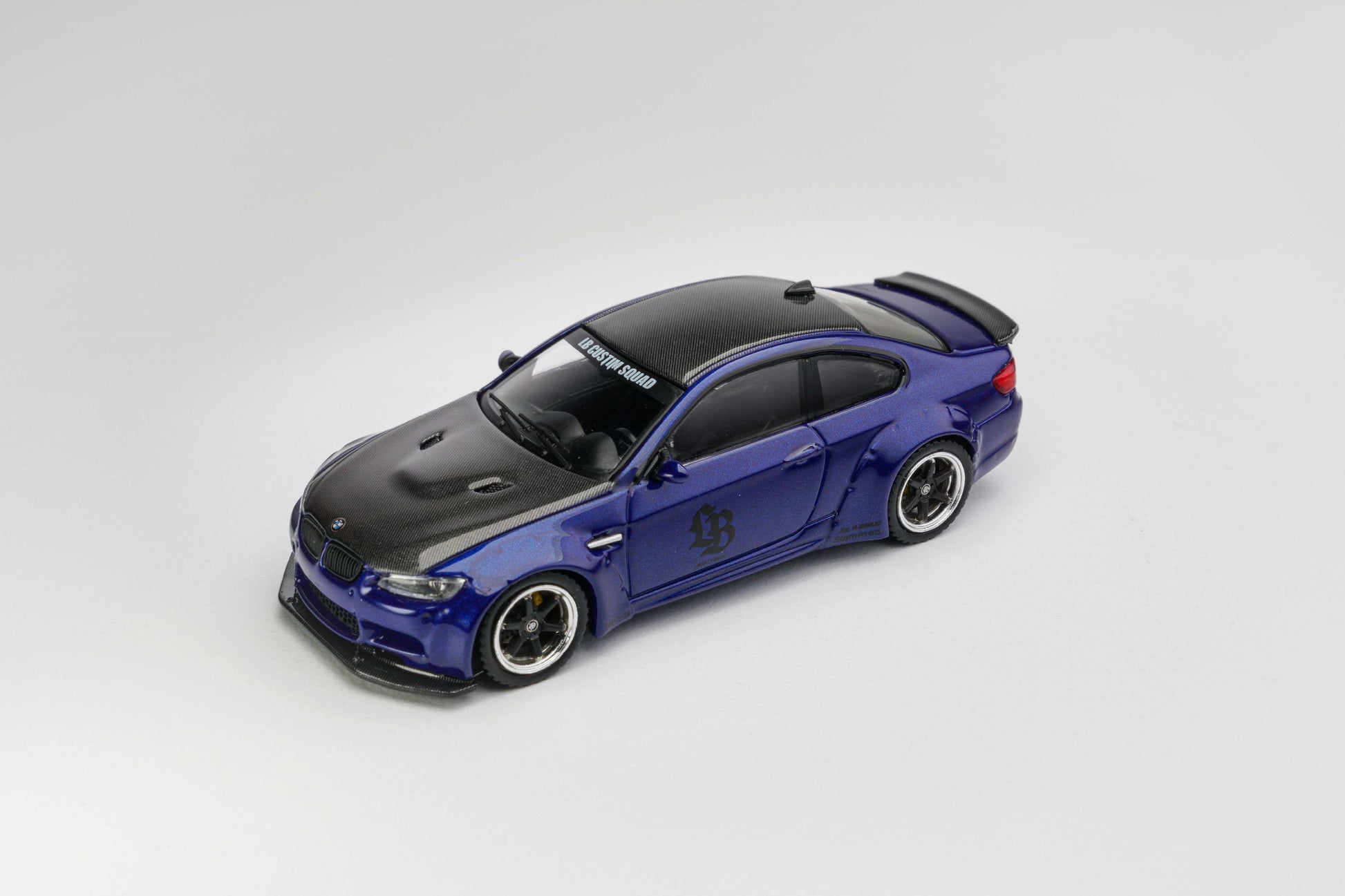 A blue and black diecast model car with a widebody stance, displayed on a clean light gray background.