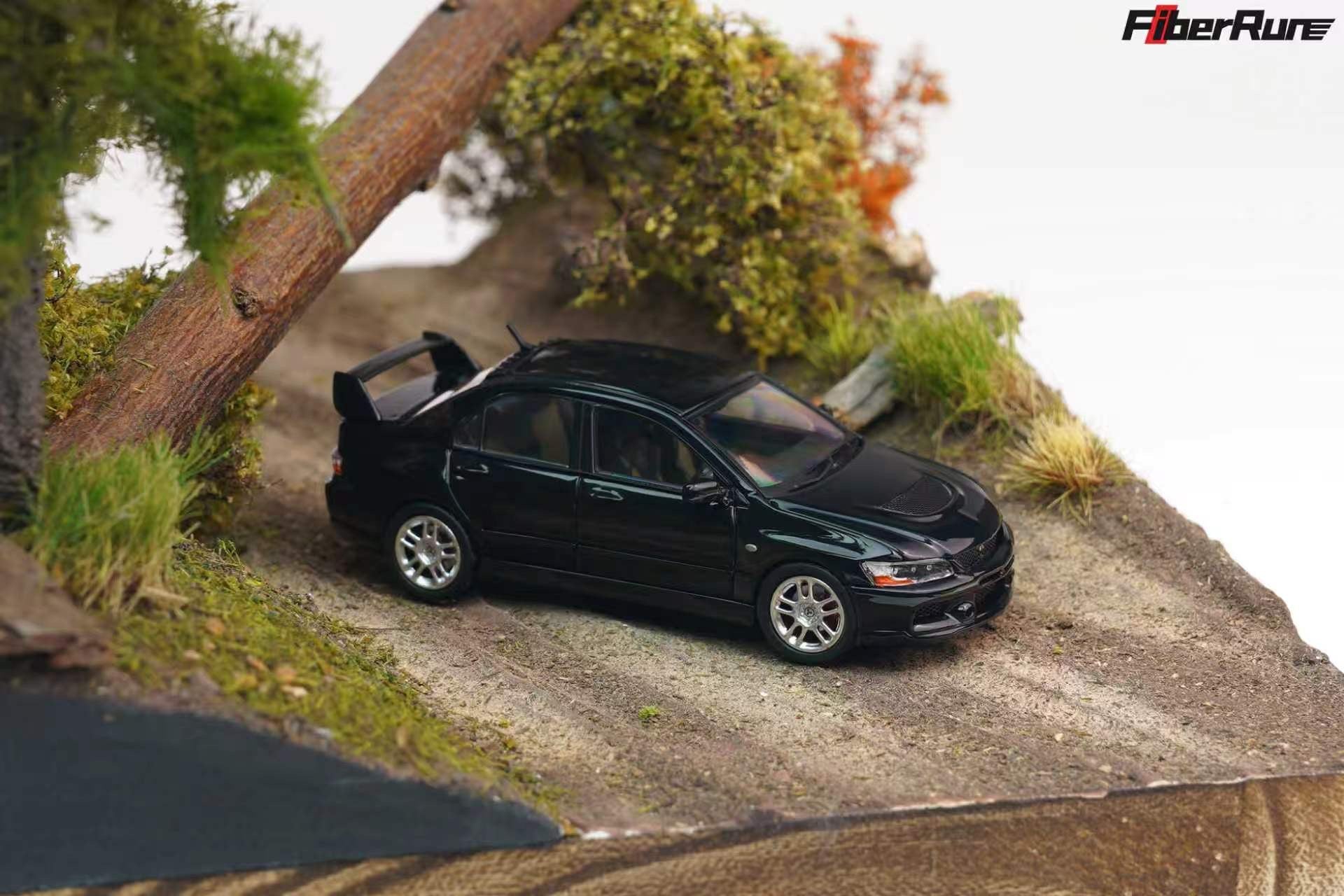 A black diecast model car with a rear spoiler, positioned on a miniature dirt road within a diorama landscape featuring grass, a tree trunk, and a white background. The FiberRun logo is visible in the top right corner.