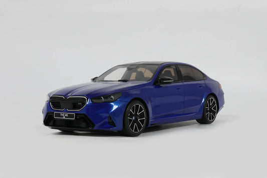A 1:18 scale model of a BMW M5 in Marina Bay Blue Metallic color, placed on a white surface.