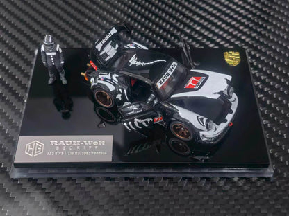 A 1:64 scale model car of a black and white Porsche 911 RSR race car, displayed on a black acrylic base with a small driver figurine. The model is branded by RAUH-Welt and features Porsche branding.