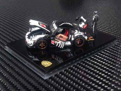 A black and white diecast model Porsche 911 Carrera RSR with orange wheels, displayed on a black base with a gold crest, set against a carbon fiber textured background.