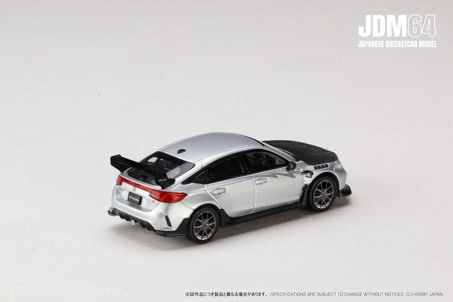 A silver diecast model car with a black hood and rear spoiler, set on a plain white background. The car is a JDM64 Japanese model.