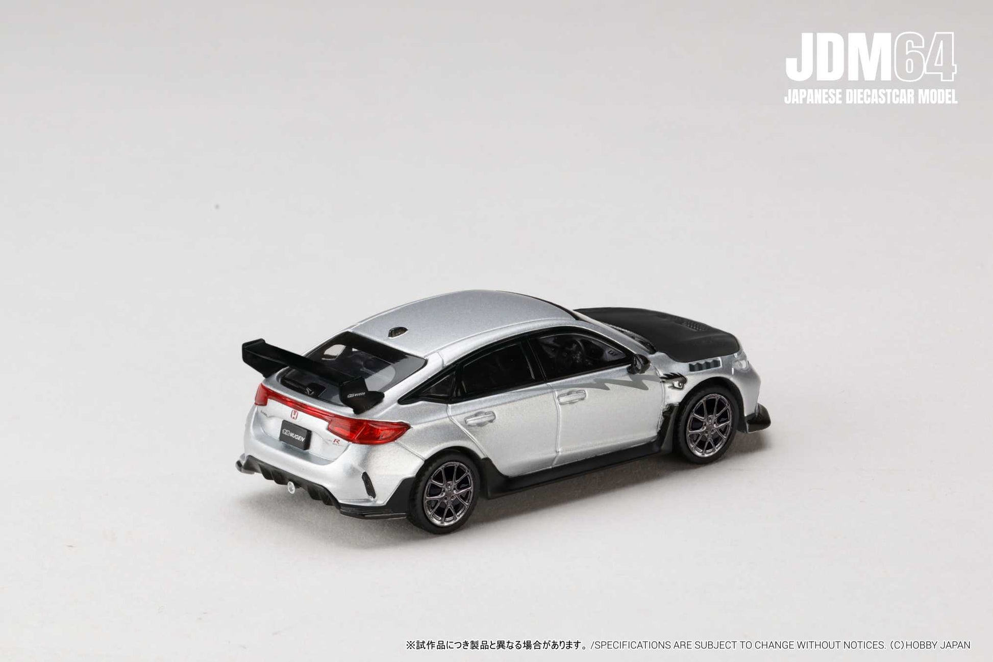 A silver diecast model car with a black hood and rear spoiler, set on a plain white background. The car is a JDM64 Japanese model.
