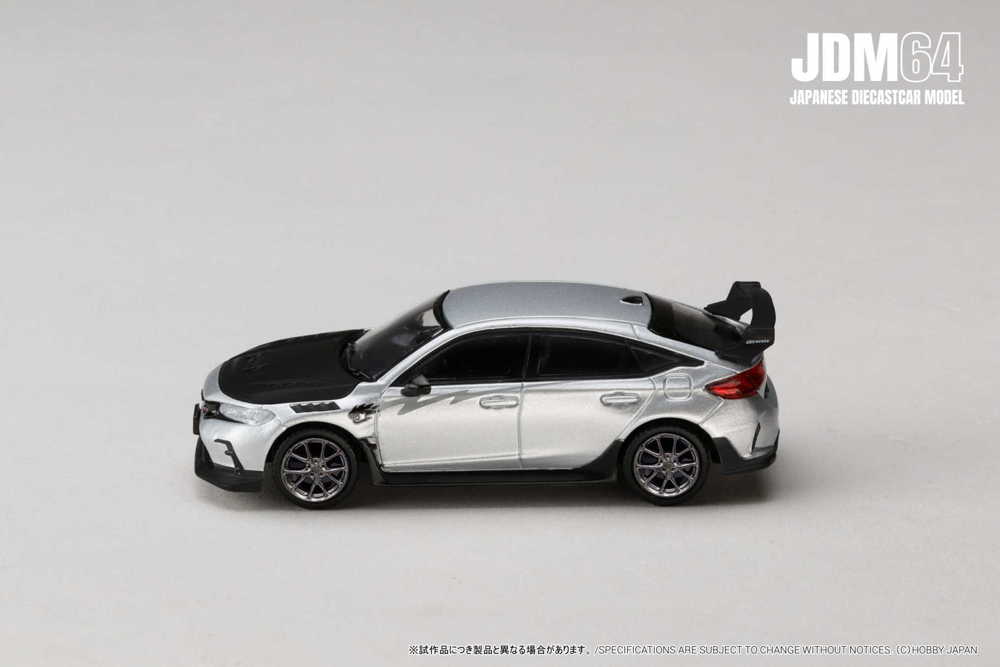 Silver and black diecast model car on a pale background, featuring sporty design with spoiler. Emphasizes sleek lines, modern aesthetic. JDM branding in corner.