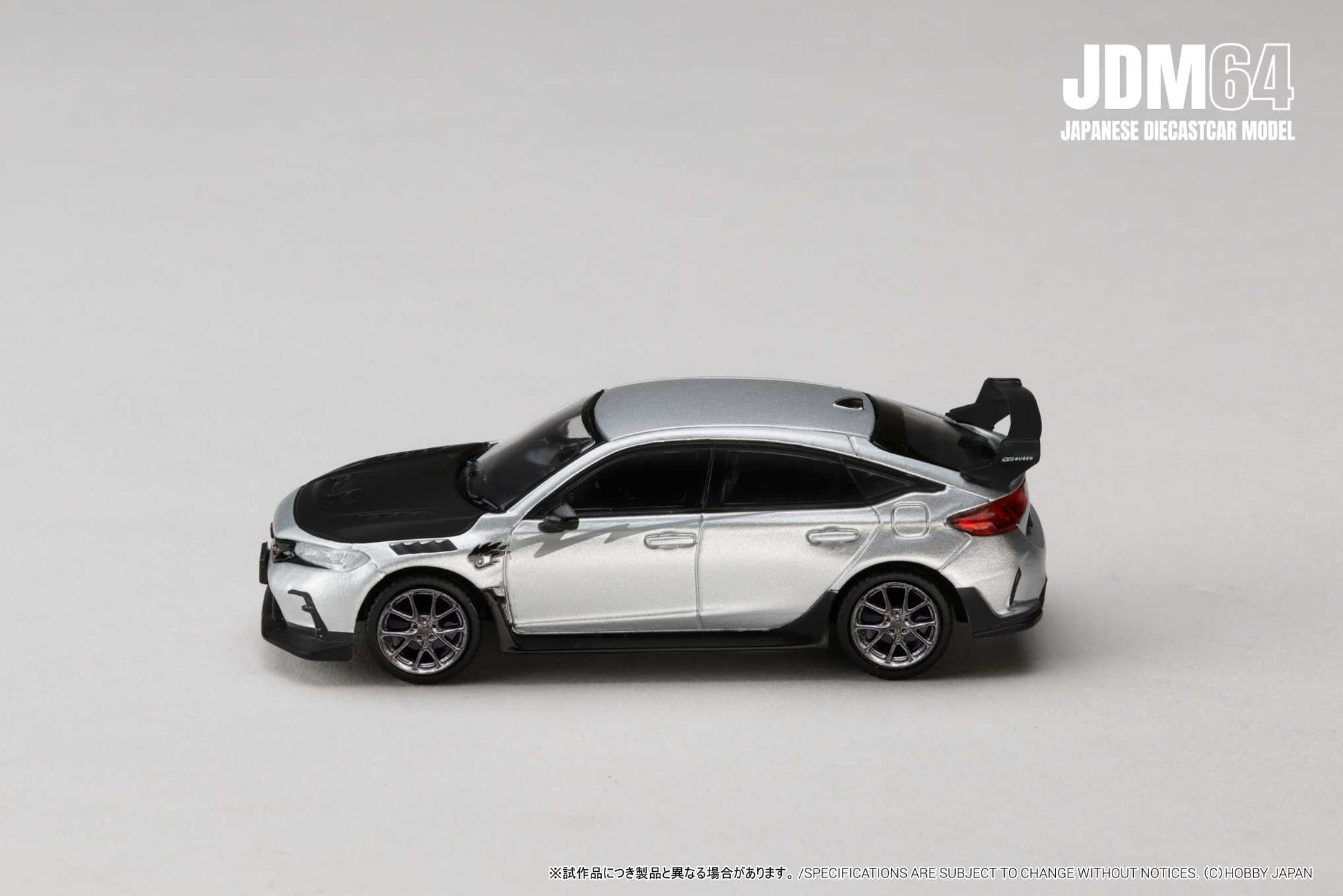 Silver and black diecast model car on a pale background, featuring sporty design with spoiler. Emphasizes sleek lines, modern aesthetic. JDM branding in corner.
