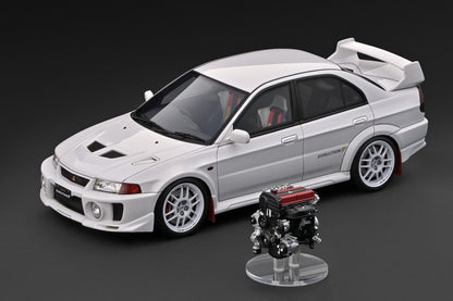 A white model car with a large rear spoiler and a small engine display stand in front, photographed on a dark gray studio background.