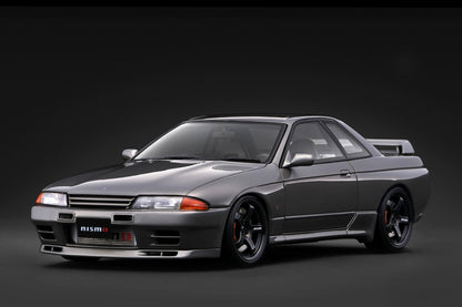A dark gray Nissan R32 GT coupe with a black hood and custom black wheels, photographed from a three-quarter front angle against a dark studio background.