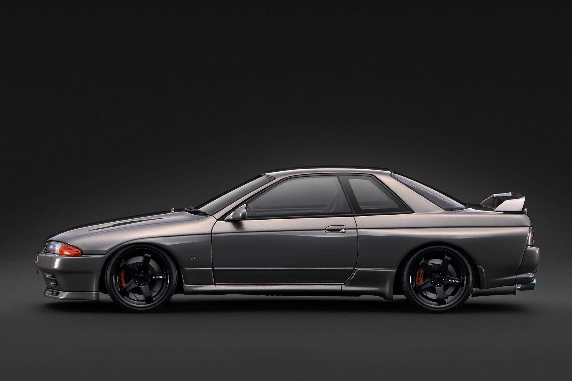 A metallic dark gray Nissan Skyline R32 GT coupe car shown in a side profile against a dark studio background.