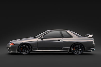 A metallic dark gray Nissan Skyline R32 GT coupe car shown in a side profile against a dark studio background.