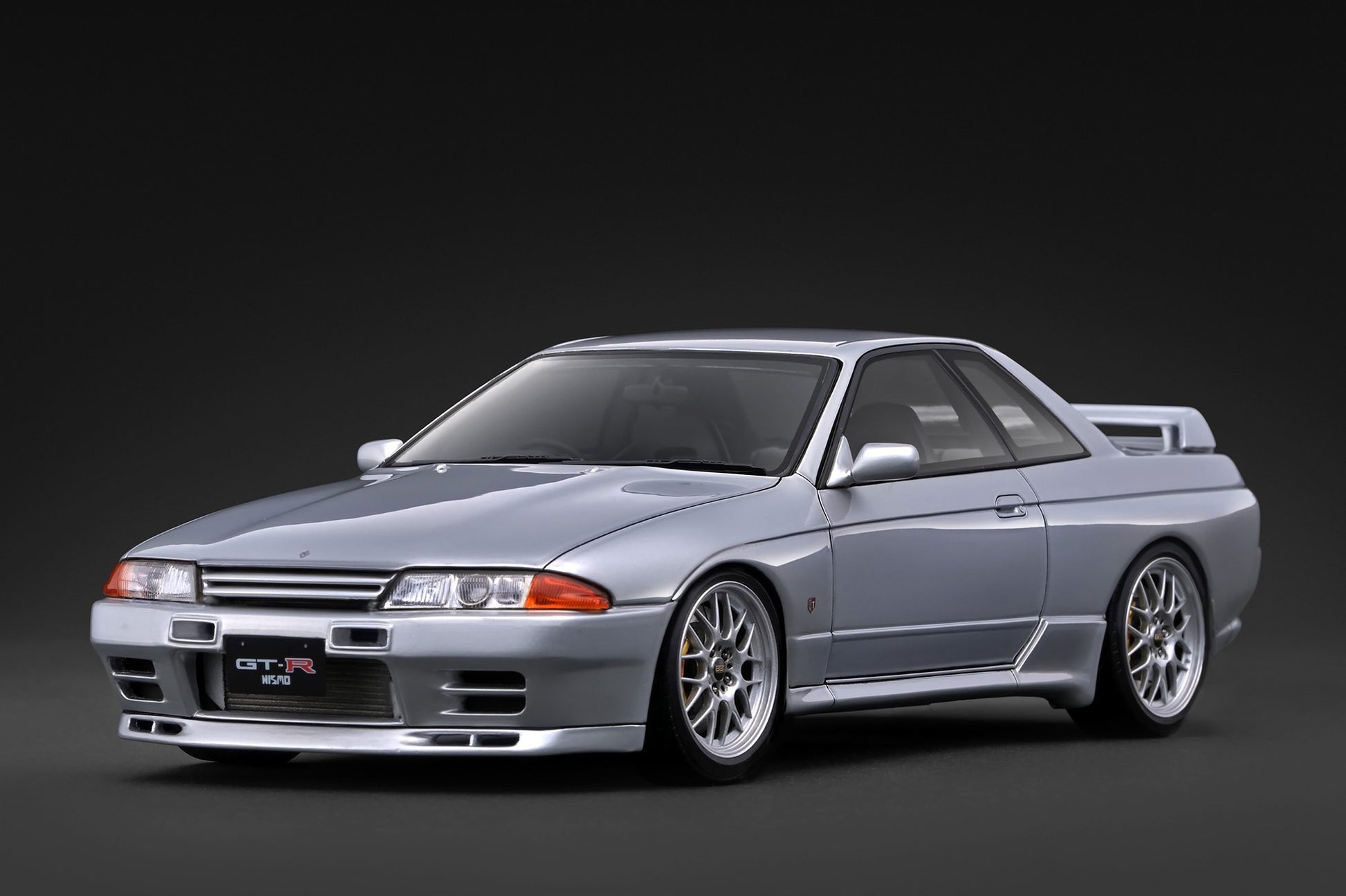 A silver Nissan GT-R R32 sports coupe shown from a three-quarter front angle on a dark studio background.