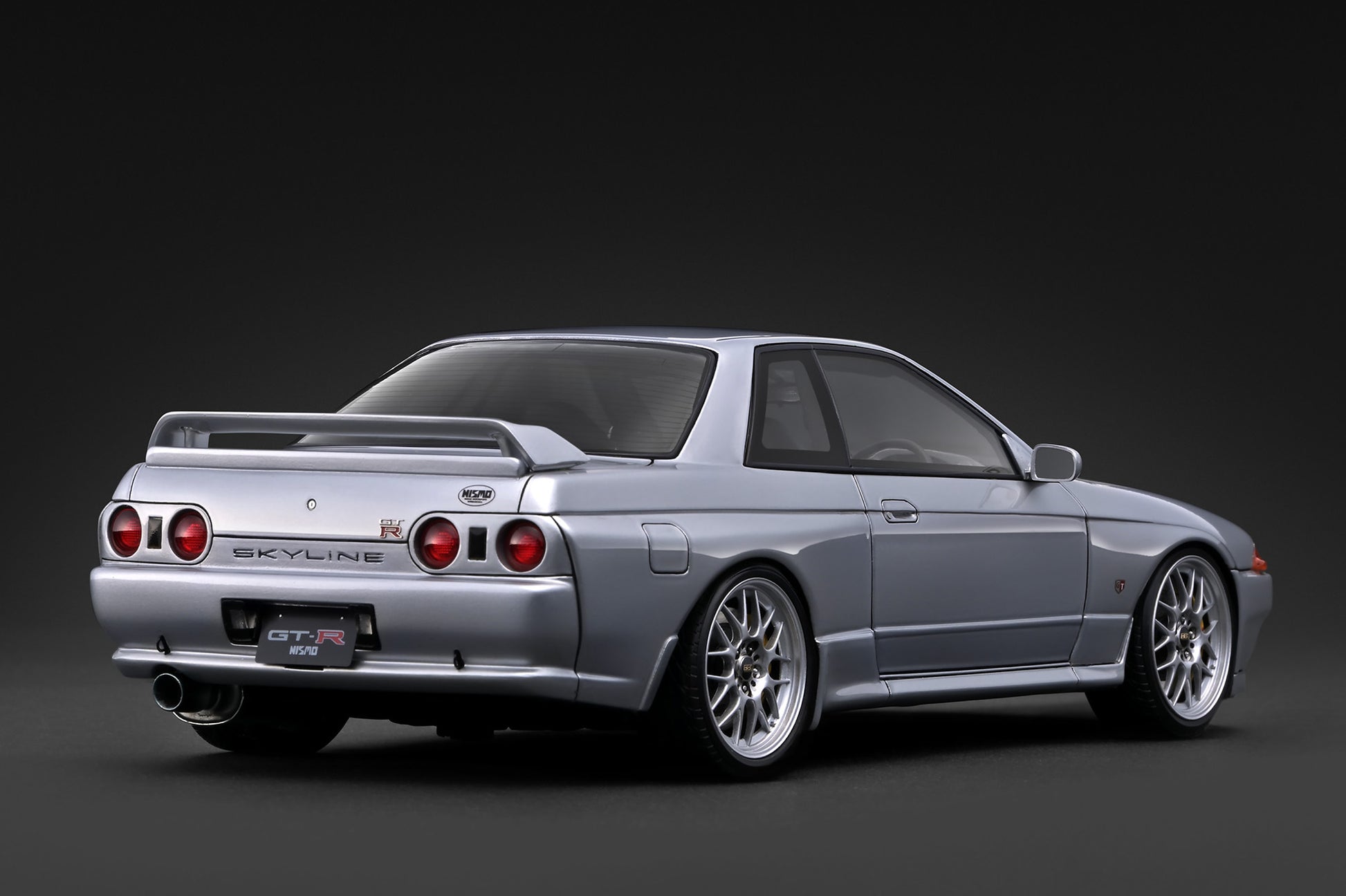 A silver Nissan Skyline R32 GT-R sports car shown from a rear three-quarter angle against a dark studio background.