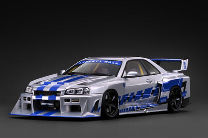 A scale model of a silver and blue Liberty Walk Nissan Skyline R32 race car, shown from a three-quarters front angle on a dark gray studio background.