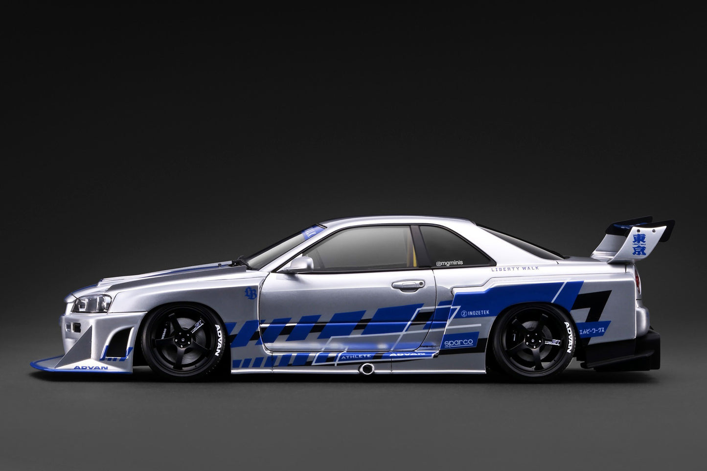 A silver Nissan R32 GT race car with blue and black graphics, shown in a side profile against a dark studio background.