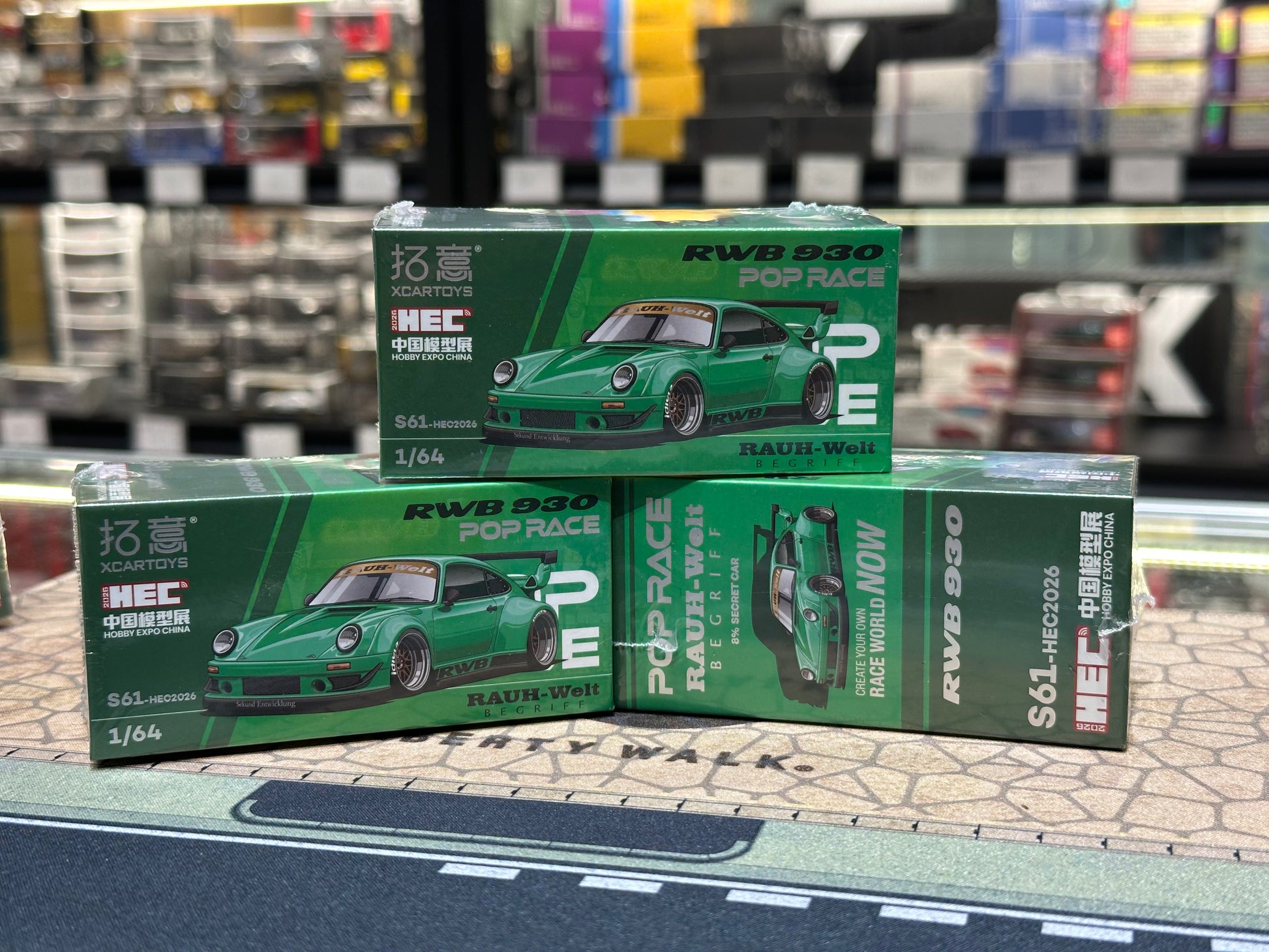 Three green model car boxes with 'RWB 930' branding on a track-themed surface.