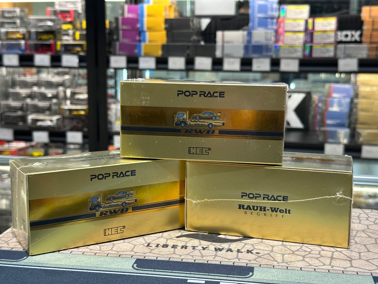 Gold boxes with 'Pop Race' branding on a counter in a store setting. The box includes Chrome Gold RWB 930 and pandem fuso-300
