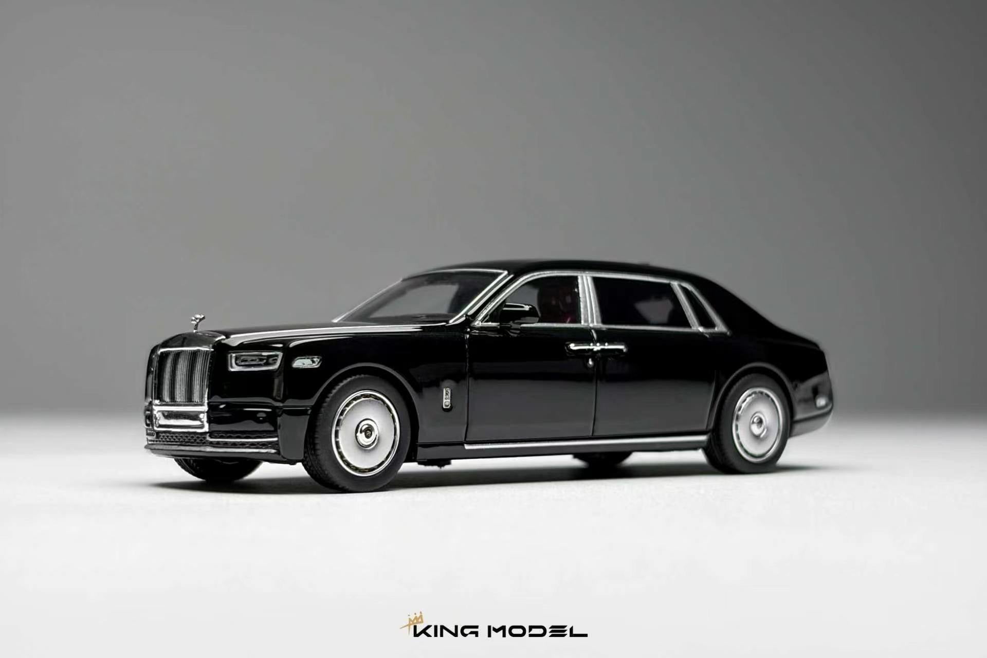 A black diecast model car of a luxury sedan, styled like a Rolls-Royce, shown from a three-quarters front angle on a neutral gray studio background. The model features chrome wheels, silver trim, and a detailed grille.
