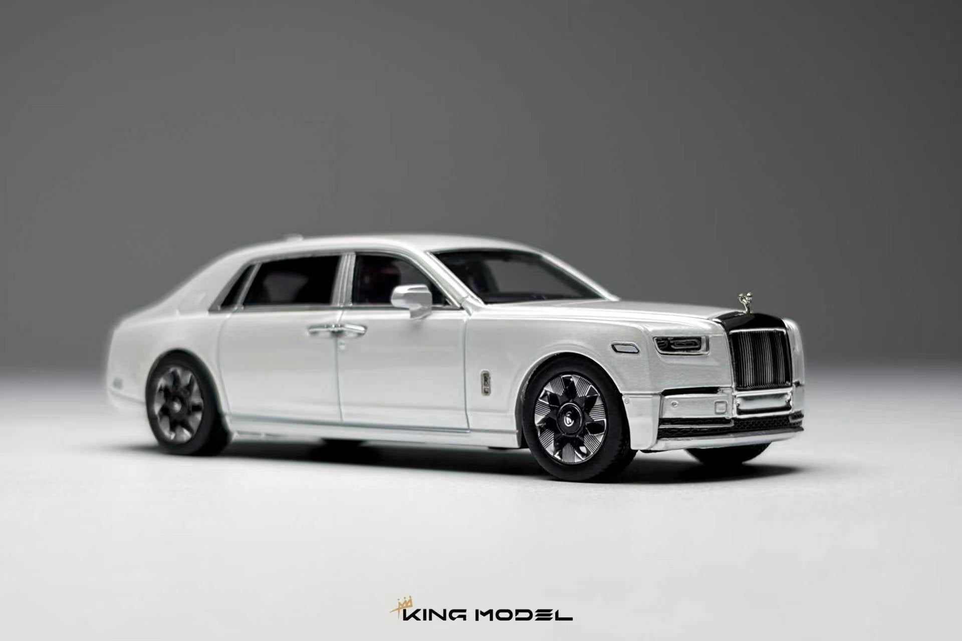 A white diecast model of a Rolls-Royce Ghost limousine, shown from a three-quarters front angle on a neutral gray studio background. The model features chrome details, black wheels, and a silver Spirit of London grille.