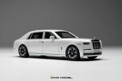 A white diecast model of a Rolls-Royce Ghost limousine, shown from a three-quarters front angle on a neutral gray studio background. The model features chrome details, black wheels, and a silver Spirit of London grille.