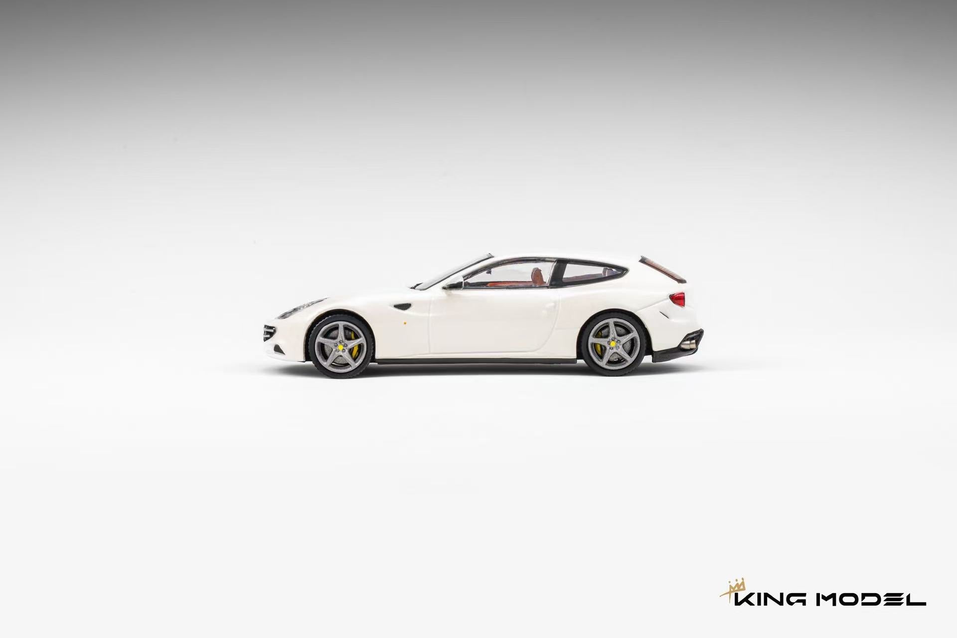 A white diecast model car, resembling a Ferrari FF, shown in a side profile on a light gray gradient background. The model features silver multi-spoke wheels and a small red accent on the rear side.