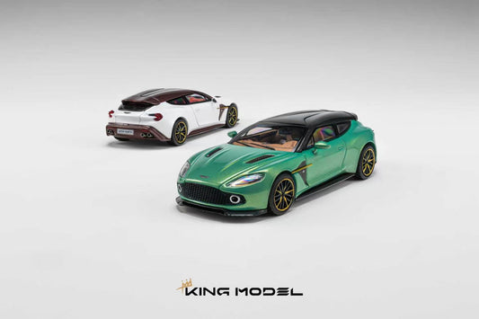 Two scale model sports cars on a light gray studio background. The foreground car is metallic green with a black roof and gold wheels, and the rear car is white with a dark roof and gold wheels.