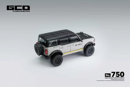 A 1/64 scale model of a GCD Air Force modified Rubicon SUV, shown from a three-quarters rear angle on a light gray gradient background. The model features a white body, a black roof and windows, black wheels, and a thin yellow stripe along the side.