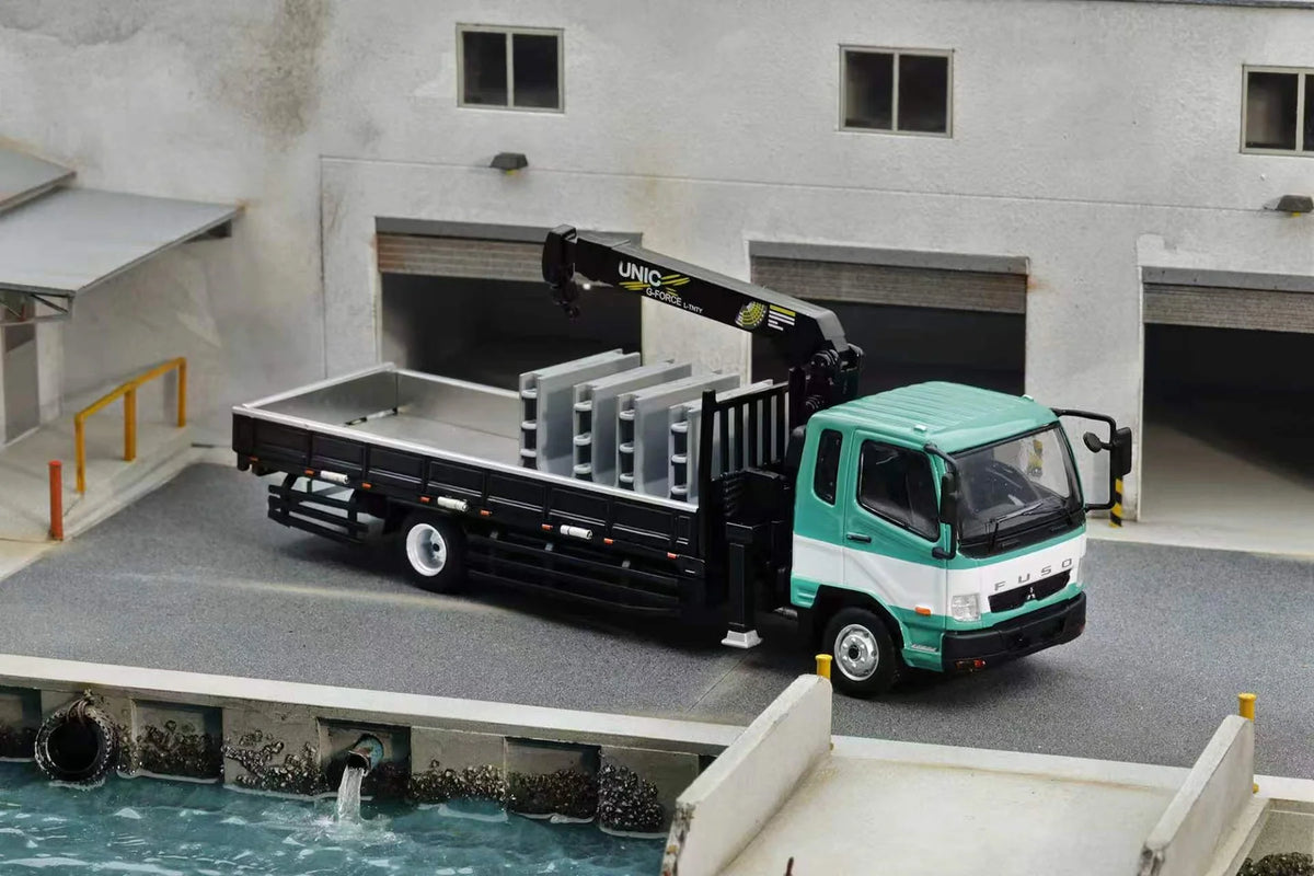GCD 1:64 Mitsubishi Fuso Fighter (1024) Flatbed Truck with UNIC Crane Green and White No.633 KS-082-633 diecast model, featuring a green and white cab, black flatbed, raised hydraulic crane, grey cargo panels, and detailed industrial warehouse diorama setting.