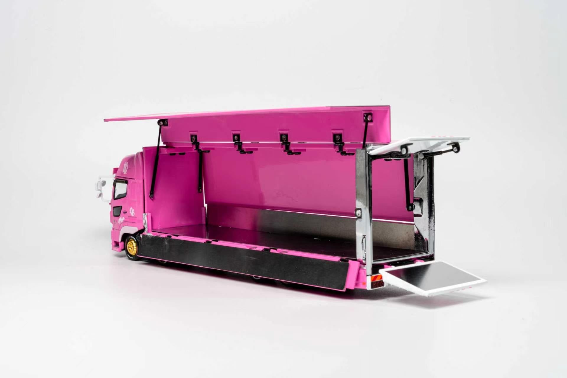 A miniature model of a pink semi-truck with its cargo bed open, featuring a bright pink interior and exterior, black lower trim, and silver metal frame details, set against a plain white studio background.