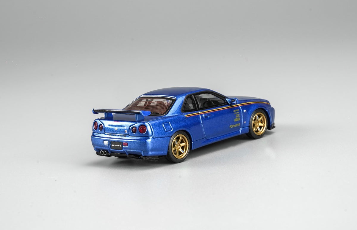 MotorHelix Nissan Skyline GT-R R34 1:64 diecast model in metallic blue, Hong Kong Toycar Salon 2026 exclusive M63453DZ-PT, rear three-quarter view with gold wheels, side graphics, rear wing and dual exhaust.