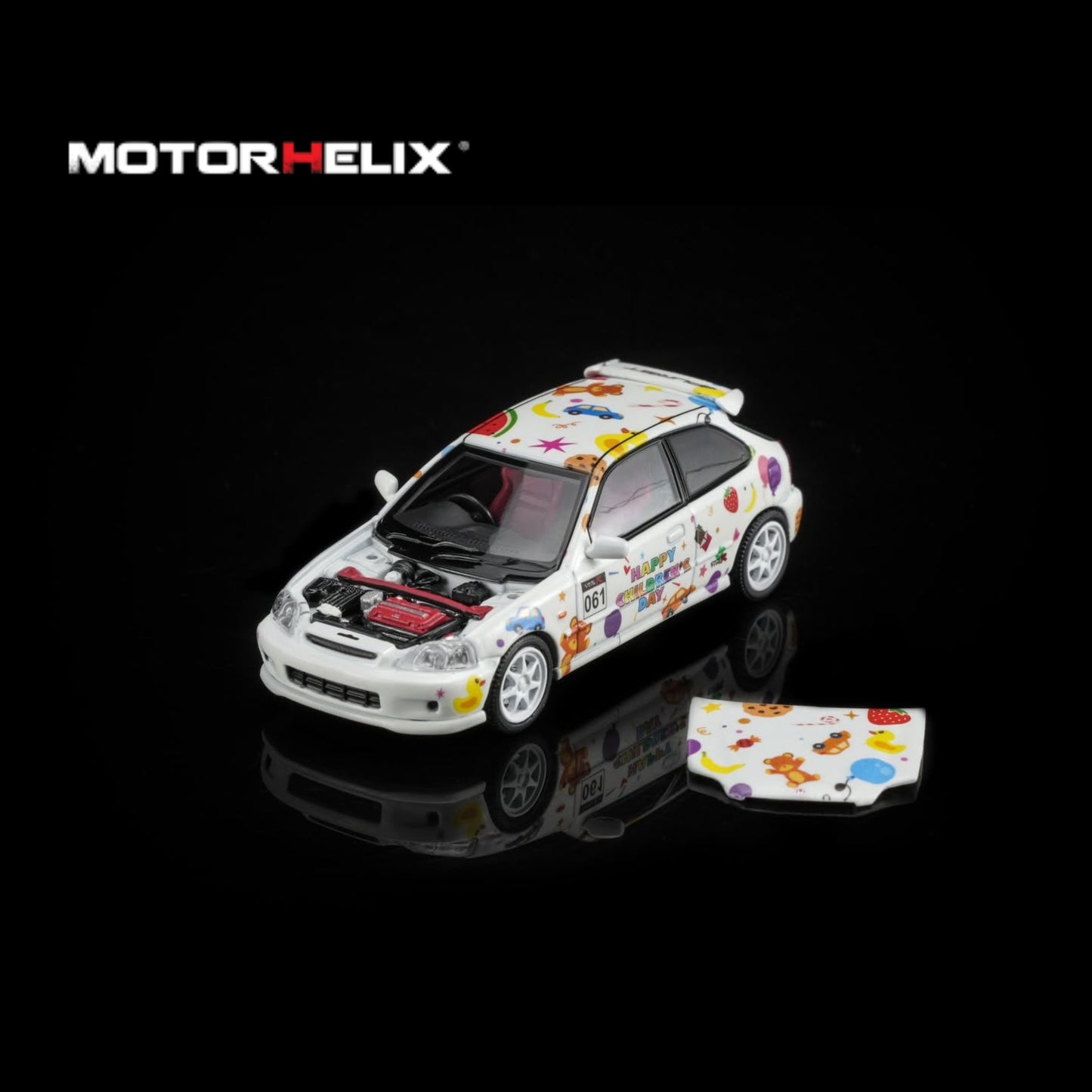A white die-cast model car with colorful cartoon decals and an open hood, shown on a black reflective background with the MOTOR HELIX logo above. A small matching decal piece lies beside the car.
