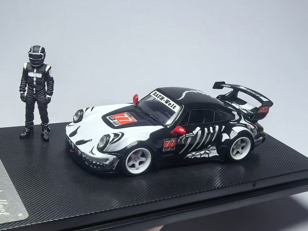 A detailed model of a black race car with white skeletal graphics, featuring "RAUH-Welt" on the windshield. A matching figure in a racing suit stands beside it.
