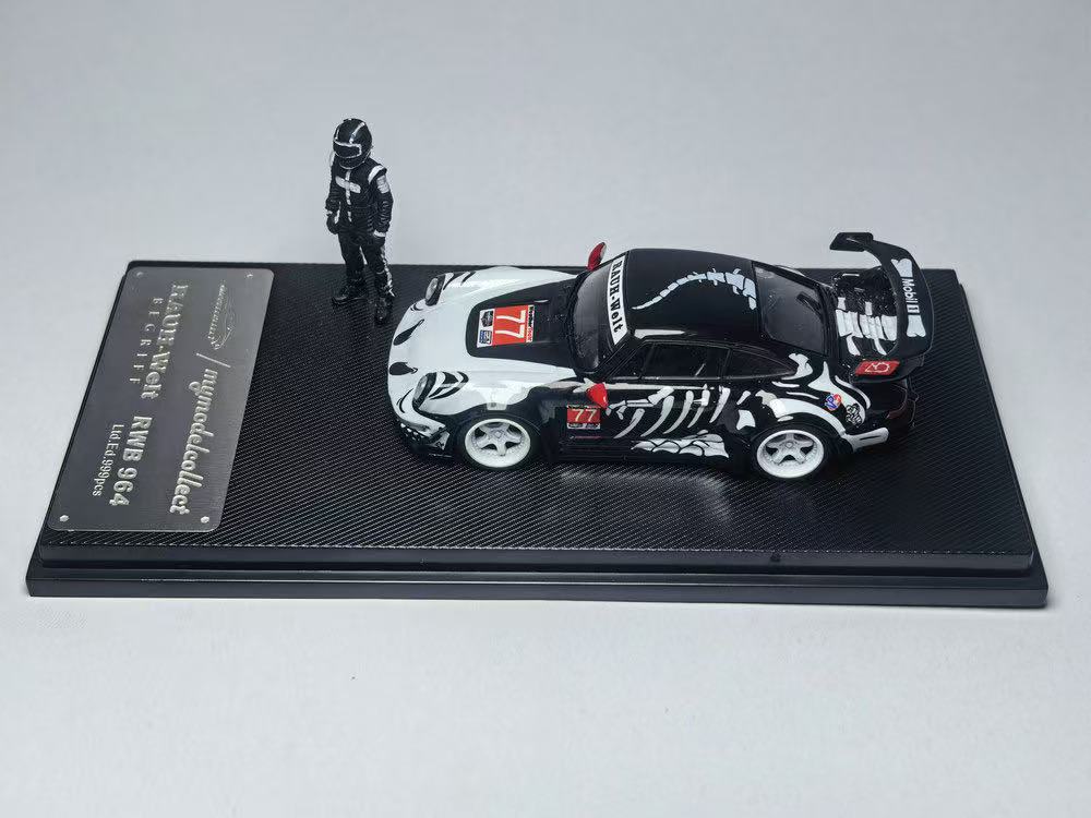 Model car with a black and white racing livery and a number 77 decal, displayed on a textured stand. A figure in a racing suit stands beside it.