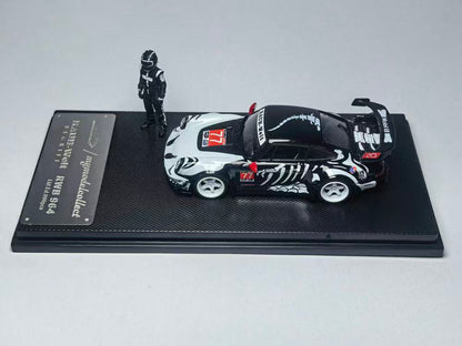 Model car with a black and white racing livery and a number 77 decal, displayed on a textured stand. A figure in a racing suit stands beside it.