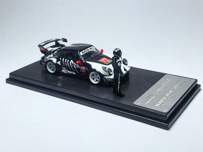 A miniature black race car with white decals and a red number 77 is displayed on a stand alongside a small helmeted driver figurine.