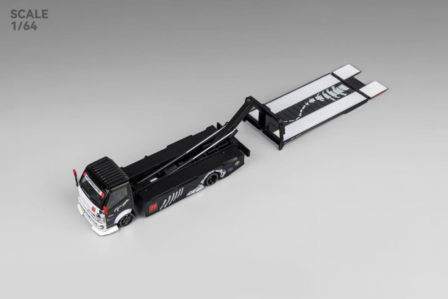 Model of a black and white car transporter truck at 1:64 scale, with extended ramp and detailed designs on the side, on a gray background.