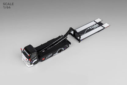 Model of a black and white car transporter truck at 1:64 scale, with extended ramp and detailed designs on the side, on a gray background.