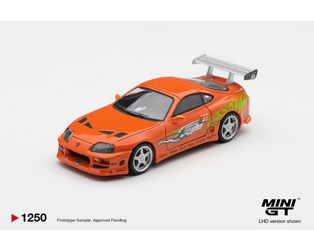 Mini GT Orange die-cast model of a Toyota Supra from "The Fast and the Furious" featuring green flame decals and a large rear spoiler on a white background.