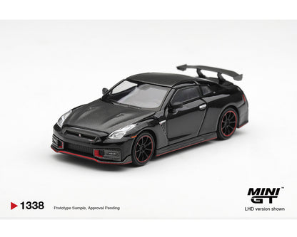 MINI GT 1:64 Nissan GT-R NISMO in gloss black featuring a carbon fiber hood, aggressive aero kit, large rear wing, black multi-spoke wheels with red accents, and red front splitter trim. Prototype diecast model shown in a front three-quarter view, LHD version, product code MGT01338-BL.