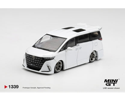 MINI GT 1:64 Toyota Alphard in pearl white featuring a lowered suspension, Modellista-style body kit, black mesh grille, silver multi-spoke deep-dish wheels, dual sunroofs, and rear spoiler. Prototype diecast model shown in a front three-quarter view, LHD version, product code MGT01339-BL.