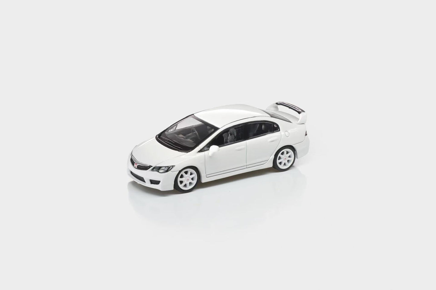 A white die-cast model car, resembling a Honda Civic, shown from a three-quarters front angle on a light gray reflective studio background.